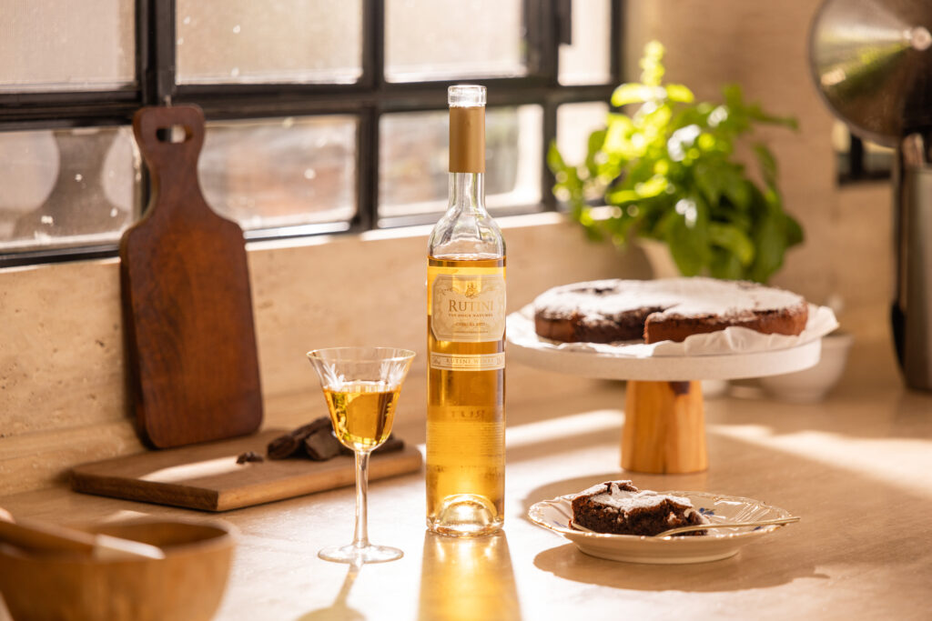 Bottle of Rutini Vin Doux Naturel next to a glass and a flourless chocolate cake