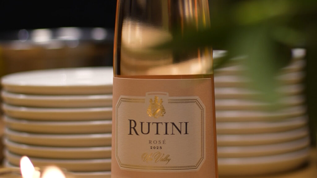 Botella de Rutini Colección Rosé de Malbec sobre una mesa iluminada por el reflejo de la ventana junto a una copa servida.