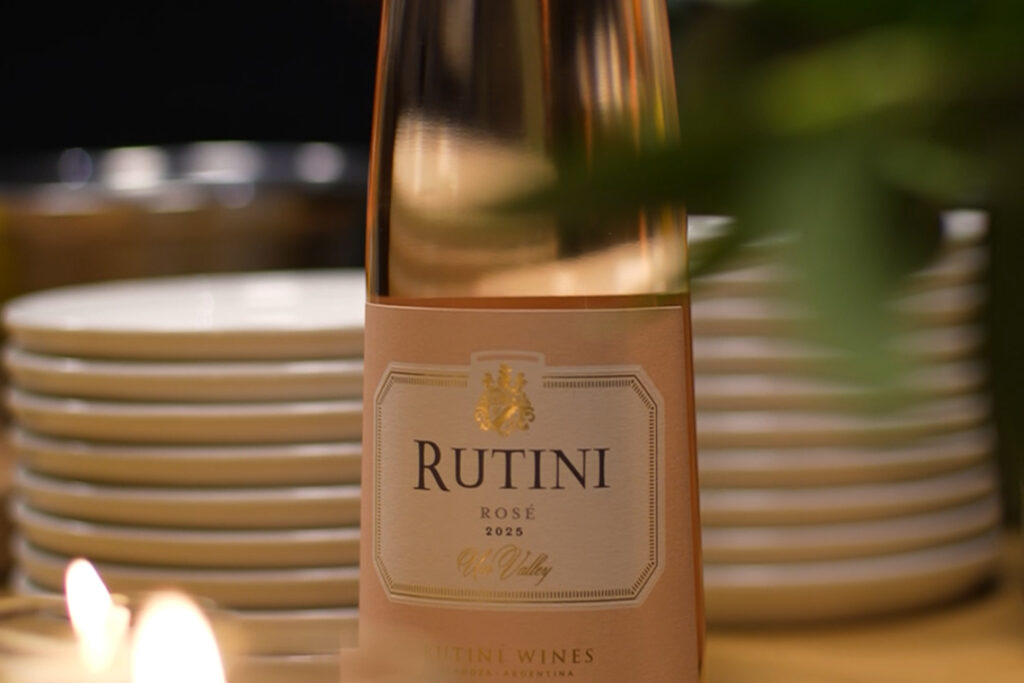 Botella de Rutini Colección Rosé de Malbec sobre una mesa iluminada por el reflejo de la ventana junto a una copa servida.